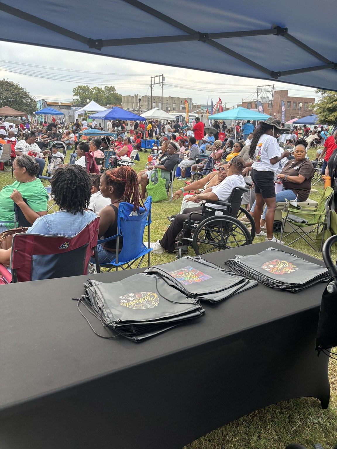 A daytime festival gathering with community members and event bags